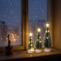 Drie kleine kerstboompjes met warmwit licht naast elkaar